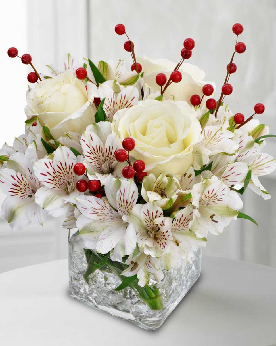 White Christmas Standard (in a 4 x 4 in Cube) White Alstroemaria, White Roses, and Red Berry Strands are arranged in a Cube Vase that is Decorated at its base with Clear Rock Acrylic.
DELIVERY: Every order is hand-delivered direct to the recipient. These items will be delivered by us locally, or a qualified retail local florist.