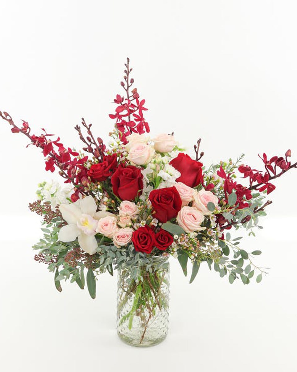 Heart and Soul Deluxe This best-selling arrangement features red roses, pink spray roses, white stock, unique Red Elephant orchids and loads of seasonal textures presented in a designer glass spin In a clear glass cylinder.