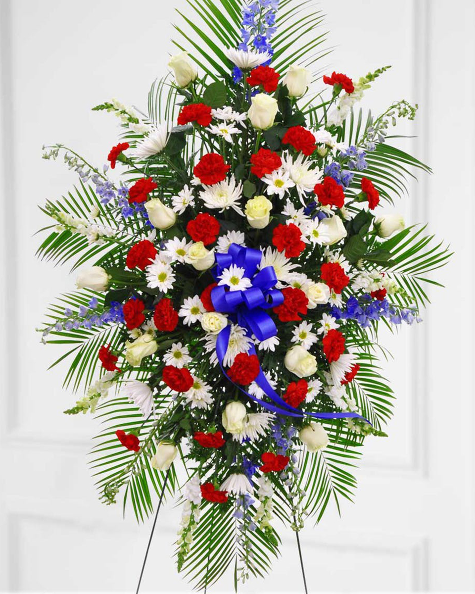 The Patriot Standard Bursting with red, white and blue, this magnificent funeral spray is intended for the truly patriotic. Commemorate a brave soldier, or pay tribute to a true American with this showy sympathy floral spray comprised of Fuji Mums, Delphinium, Carnations, Snapdragons, and more, complemented with ribbon and a touch of greenery.
DELIVERY: Every order is hand-delivered direct to the recipient. These items will be delivered by us locally, or a qualified retail local florist.