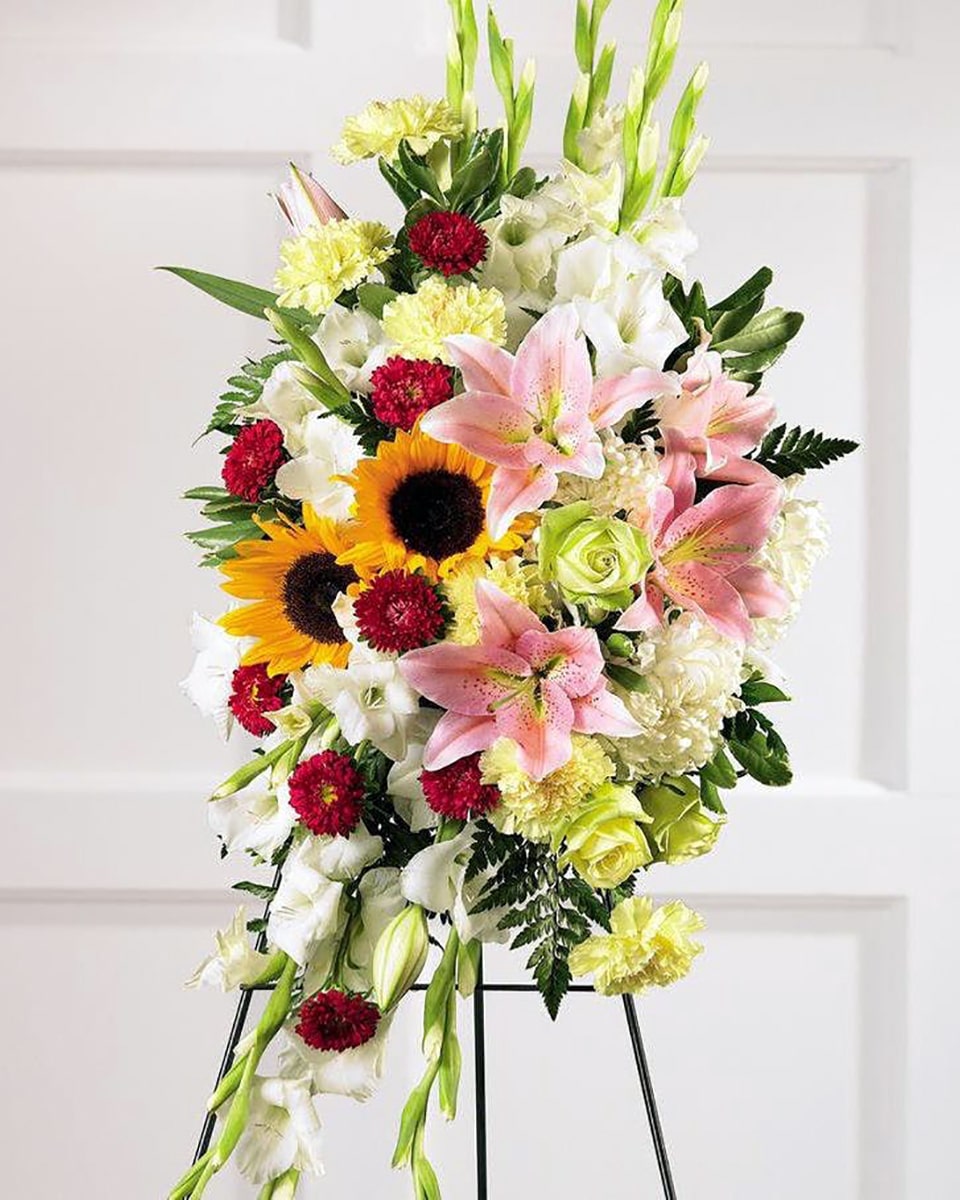 Fondest Memories Standard Stargazer lilies, yellow sunflowers, and a collection of white and light green flowers are clustered together in this beautiful spray. Arrangement is delivered on an easel and is appropriate to send to a funeral home or service.
DELIVERY: Every order is hand-delivered direct to the recipient. These items will be delivered by us locally, or a qualified retail local florist.