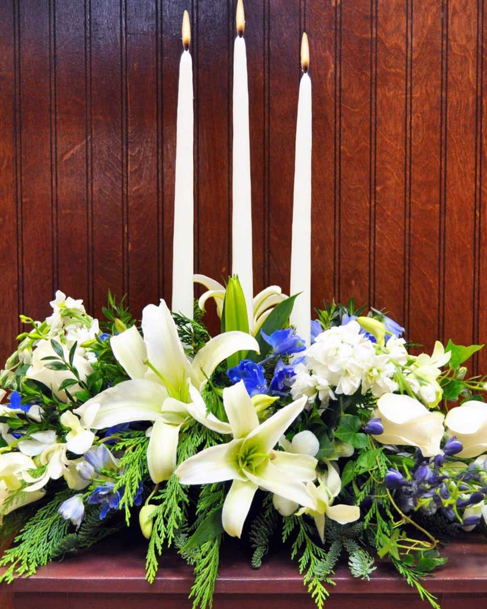 White Pastures Standard White Lilies, White Roses, White Carnations, White Dendrobium Orchids, Blue Bella Donna Delphinium, Ivy, Cedar, and 3 White Candles Comprise this Table Centerpiece.
DELIVERY: Every order is hand-delivered direct to the recipient. These items will be delivered by us locally, or a qualified retail local florist.